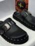 A pair of black leather Toga Pulla mule slides with silver buckles and studs, presented in a white box with the brand's logo.