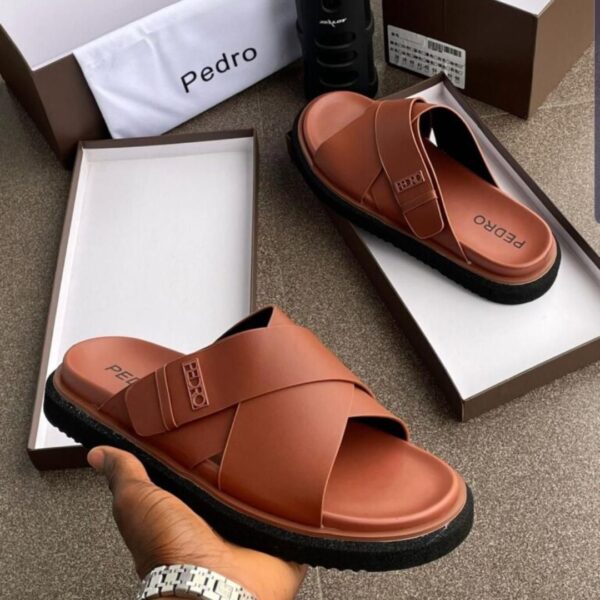 A pair of brown double strap slide sandals with black sole, presented in an open box with a luxurious setting.