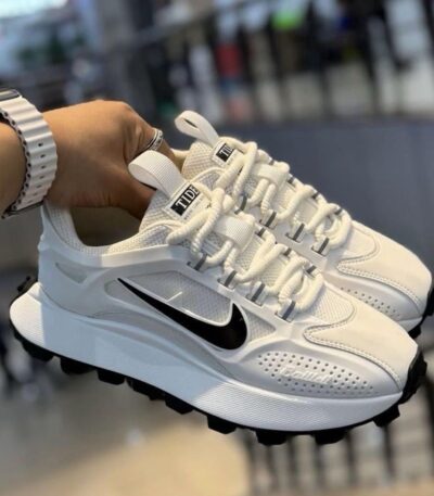 A pair of white Nike running shoes with black accents and Tide label, held by a hand with a stylish watch.
