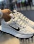A pair of white Nike running shoes with black accents and Tide label, held by a hand with a stylish watch.