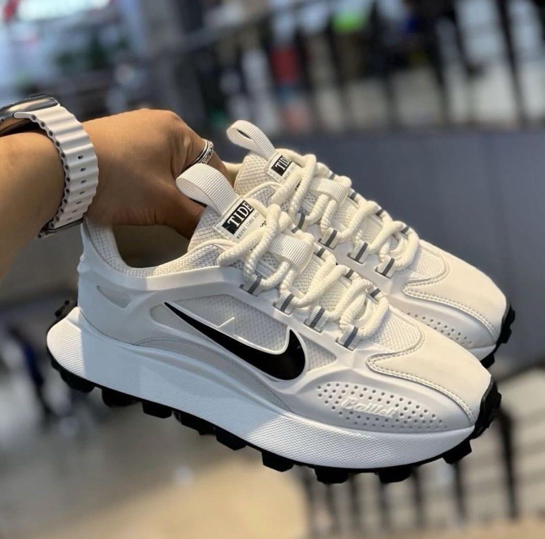 IMG-20260425-WA0008 A pair of white Nike running shoes with black accents and Tide label, held by a hand with a stylish watch.