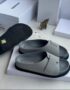 A pair of gray leather Jil Sander slide sandals with black outsole, displayed on a white box with the brand's logo and packaging in the background.