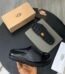 A pair of black UGG leather slide sandals with original box, dust bag, and packaging on a stylish black table.
