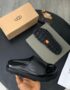 A pair of black UGG leather slide sandals with original box, dust bag, and packaging on a stylish black table.