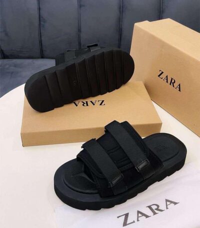 A pair of black two-strap sandals with thick rubber sole, displayed on a white table with Zara box and cloth.