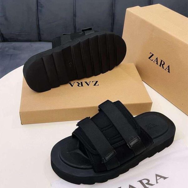 A pair of black two-strap sandals with thick rubber sole, displayed on a white table with Zara box and cloth.