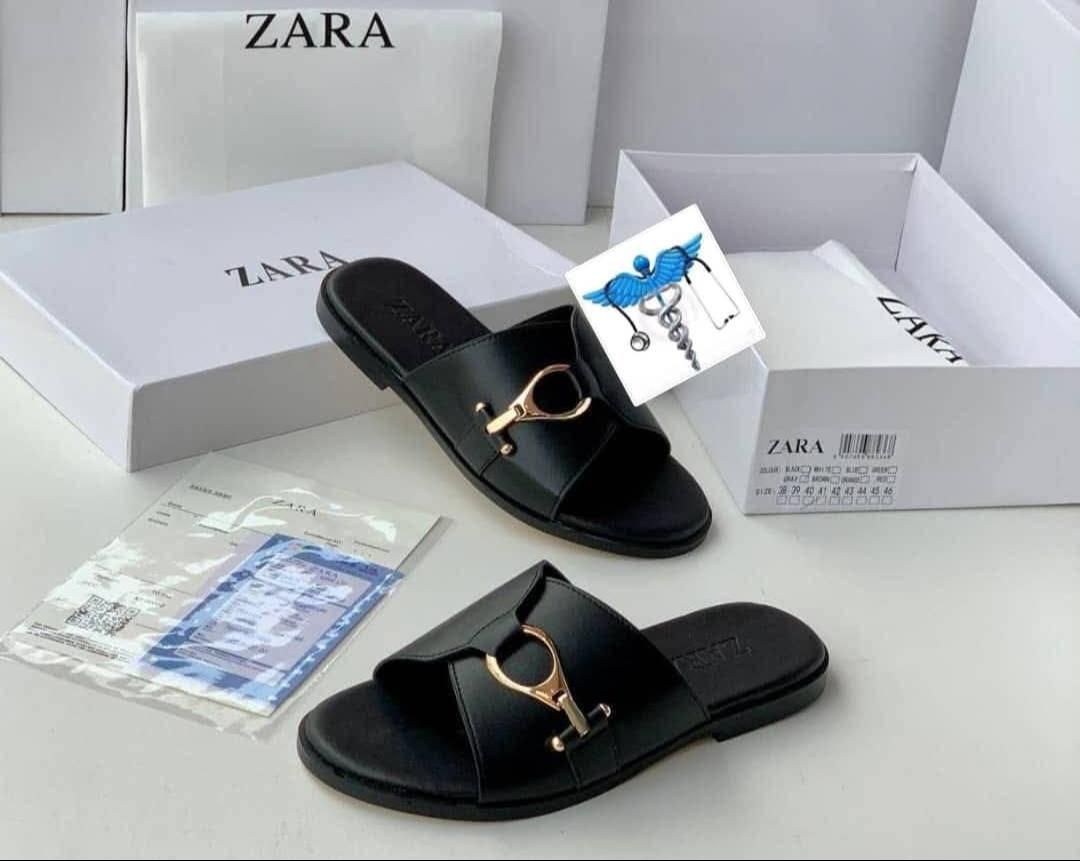 IMG-20260425-WA0020 A pair of black leather slide sandals with a gold buckle, displayed with their white box and packaging on a clean white surface.