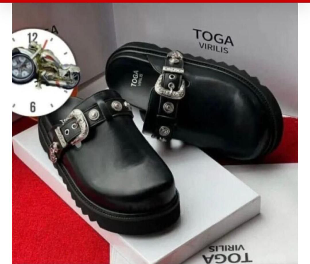IMG-20260425-WA0021 A pair of black leather clogs with silver buckles on a white box, showcasing the Toga Virilis logo, perfect for luxury footwear enthusiasts.