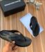 A pair of black rubber thong sandals with an embossed Alexander Wang logo, displayed on a wooden surface with the brand's box and packaging.