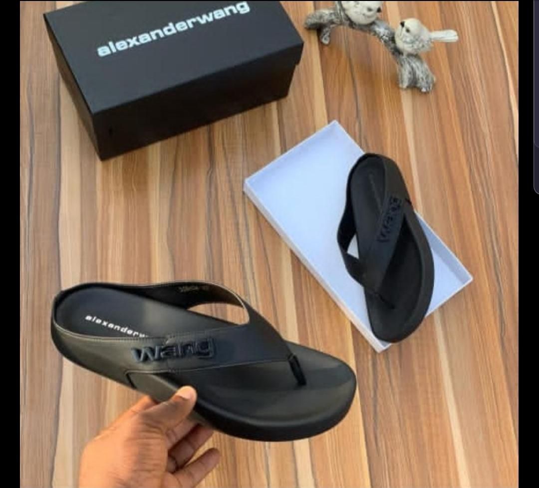 IMG-20260425-WA0022 A pair of black rubber thong sandals with an embossed Alexander Wang logo, displayed on a wooden surface with the brand's box and packaging.
