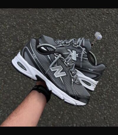 A pair of New Balance Fresh Foam 860v12 running shoes in grey and white, being held by a hand, showcasing the shoe's design and comfort features.