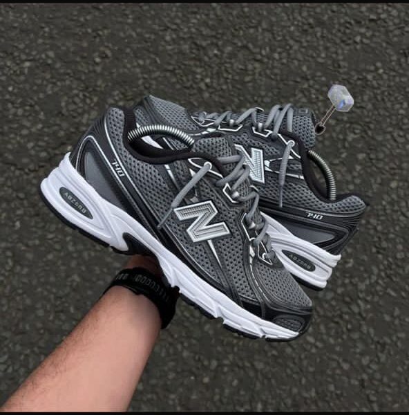 A pair of New Balance Fresh Foam 860v12 running shoes in grey and white, being held by a hand, showcasing the shoe's design and comfort features.