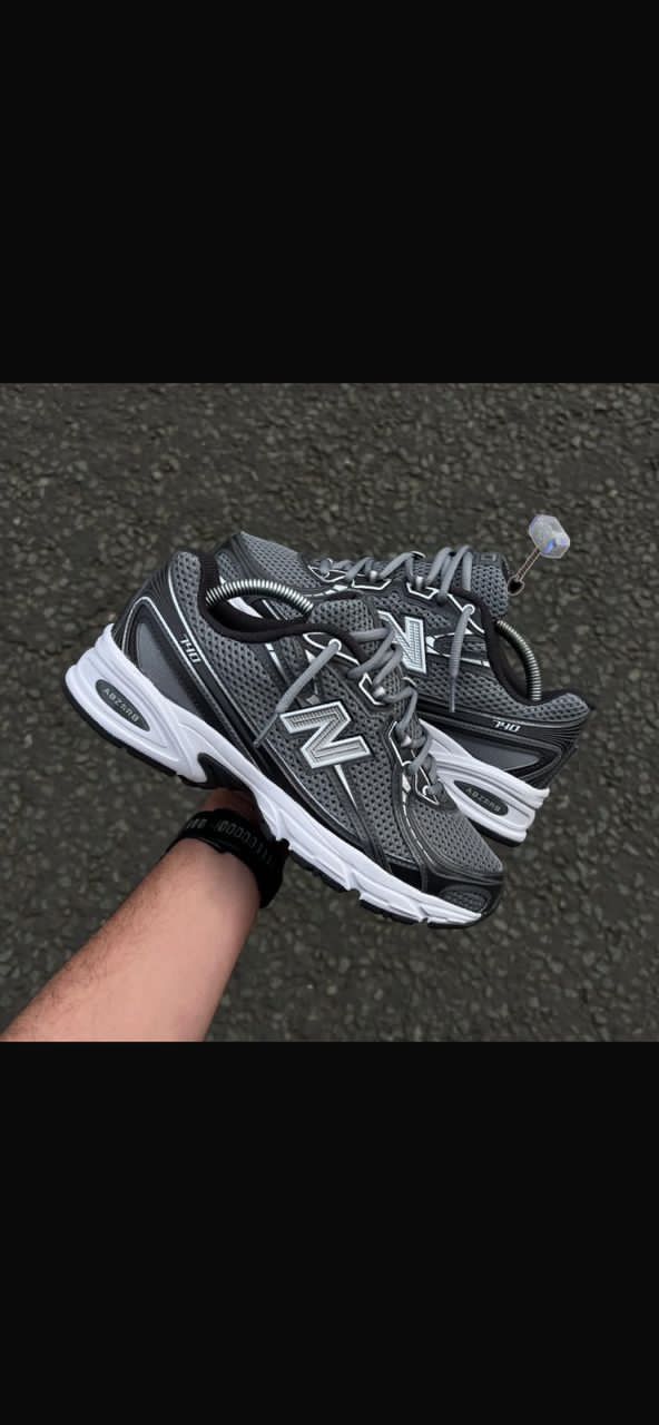 IMG-20260425-WA0023 A pair of New Balance Fresh Foam 860v12 running shoes in grey and white, being held by a hand, showcasing the shoe's design and comfort features.