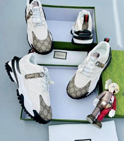 A pair of white Gucci x The North Face sneakers with monogram pattern, displayed in a green box with a small figurine.