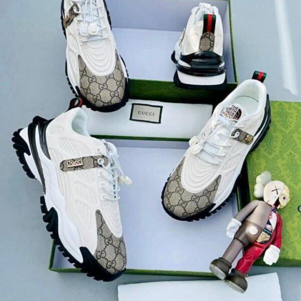 A pair of white Gucci x The North Face sneakers with monogram pattern, displayed in a green box with a small figurine.