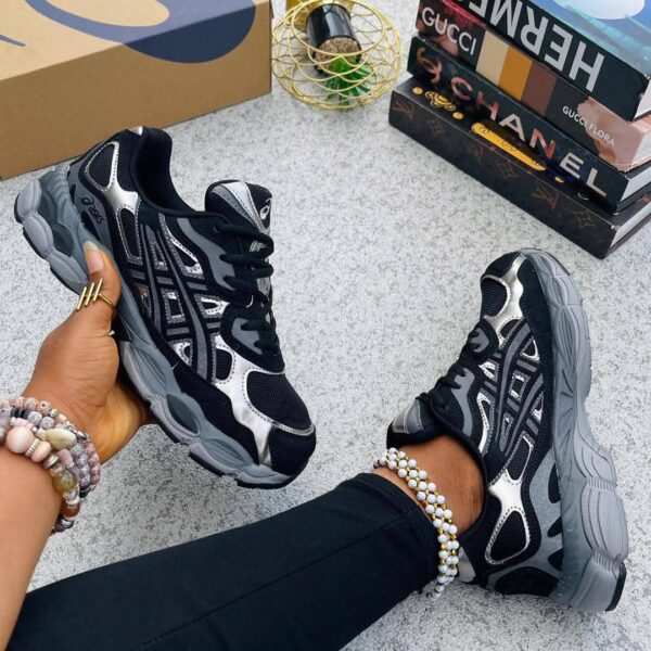 A pair of black and silver luxury sneakers on a woman's feet, with a stylish background featuring luxury brand boxes.