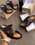 A display of black and brown double strap rubber sandals on a brown surface, with shoe boxes and a hand holding one sandal.