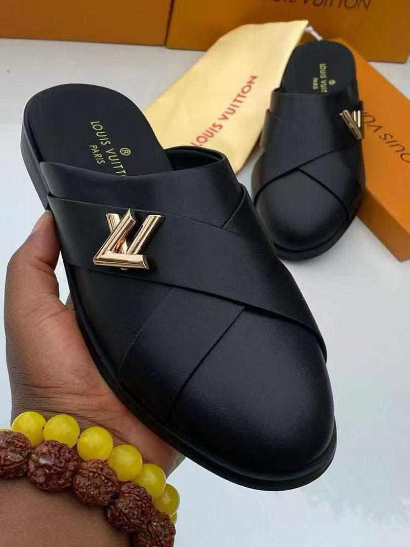 IMG-20260425-WA0032 A pair of black leather Louis Vuitton slide sandals with gold-tone logo, presented on a white surface with luxury packaging in the background.