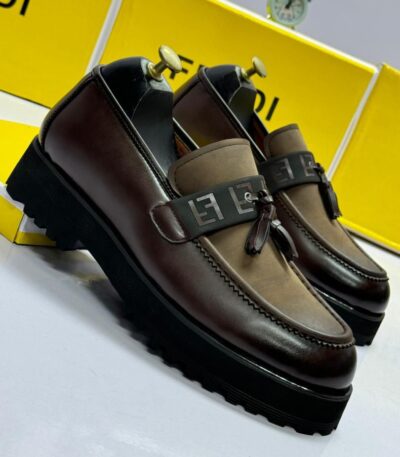 A pair of luxurious brown leather loafers with tassel details, set against a backdrop of yellow shoe boxes and a sleek alarm clock.