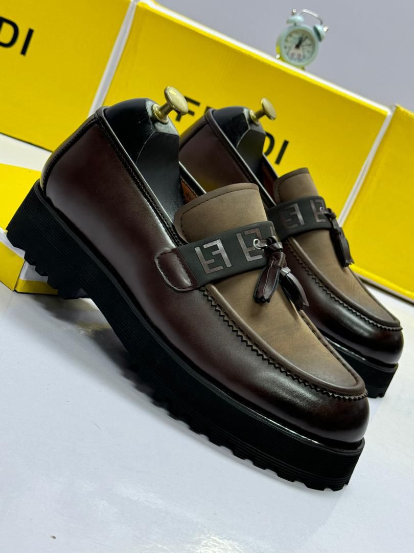 IMG-20260425-WA0033 A pair of luxurious brown leather loafers with tassel details, set against a backdrop of yellow shoe boxes and a sleek alarm clock.