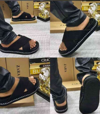 A close-up view of a person wearing black strap sandals with white stitching, showcasing the shoe from multiple angles.