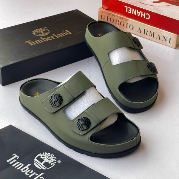 A pair of olive green Timberland sandals with black soles and logo buckles, displayed with their box and packaging on a white surface.