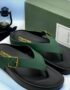 A pair of luxurious green leather thong sandals with gold buckle and TOMFORD branding, displayed on a white surface with a green shoe box and lantern in the background.