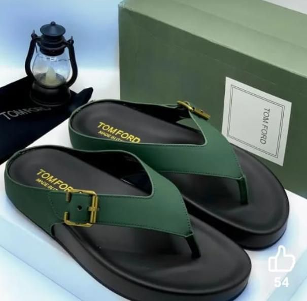 IMG-20260425-WA0037 A pair of luxurious green leather thong sandals with gold buckle and TOMFORD branding, displayed on a white surface with a green shoe box and lantern in the background.