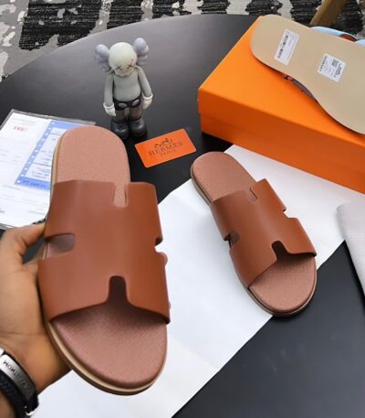 A pair of luxurious brown leather sandals from Hermes Paris, displayed on a table with their box and accessories, showcasing the brand's signature style and attention to detail.