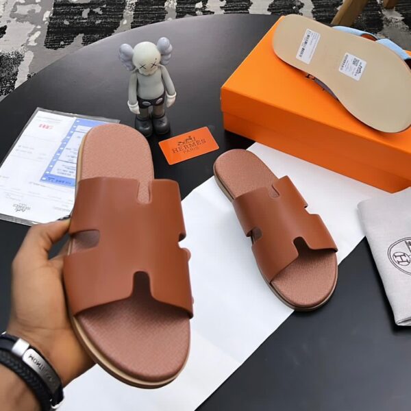 A pair of luxurious brown leather sandals from Hermes Paris, displayed on a table with their box and accessories, showcasing the brand's signature style and attention to detail.