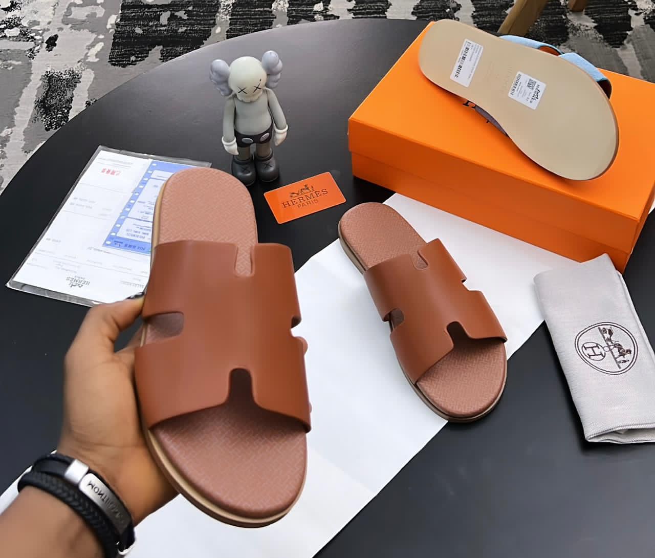 IMG-20260425-WA0039 A pair of luxurious brown leather sandals from Hermes Paris, displayed on a table with their box and accessories, showcasing the brand's signature style and attention to detail.