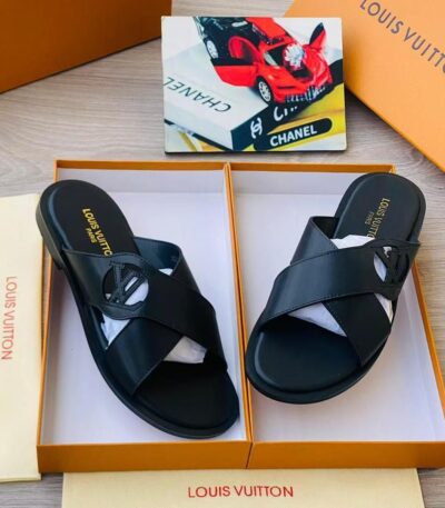 A pair of black leather Louis Vuitton slide sandals with gold-toned logo, presented in an open orange box with white interior and accompanied by a dust bag.