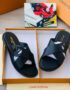 A pair of black leather Louis Vuitton slide sandals with gold-toned logo, presented in an open orange box with white interior and accompanied by a dust bag.