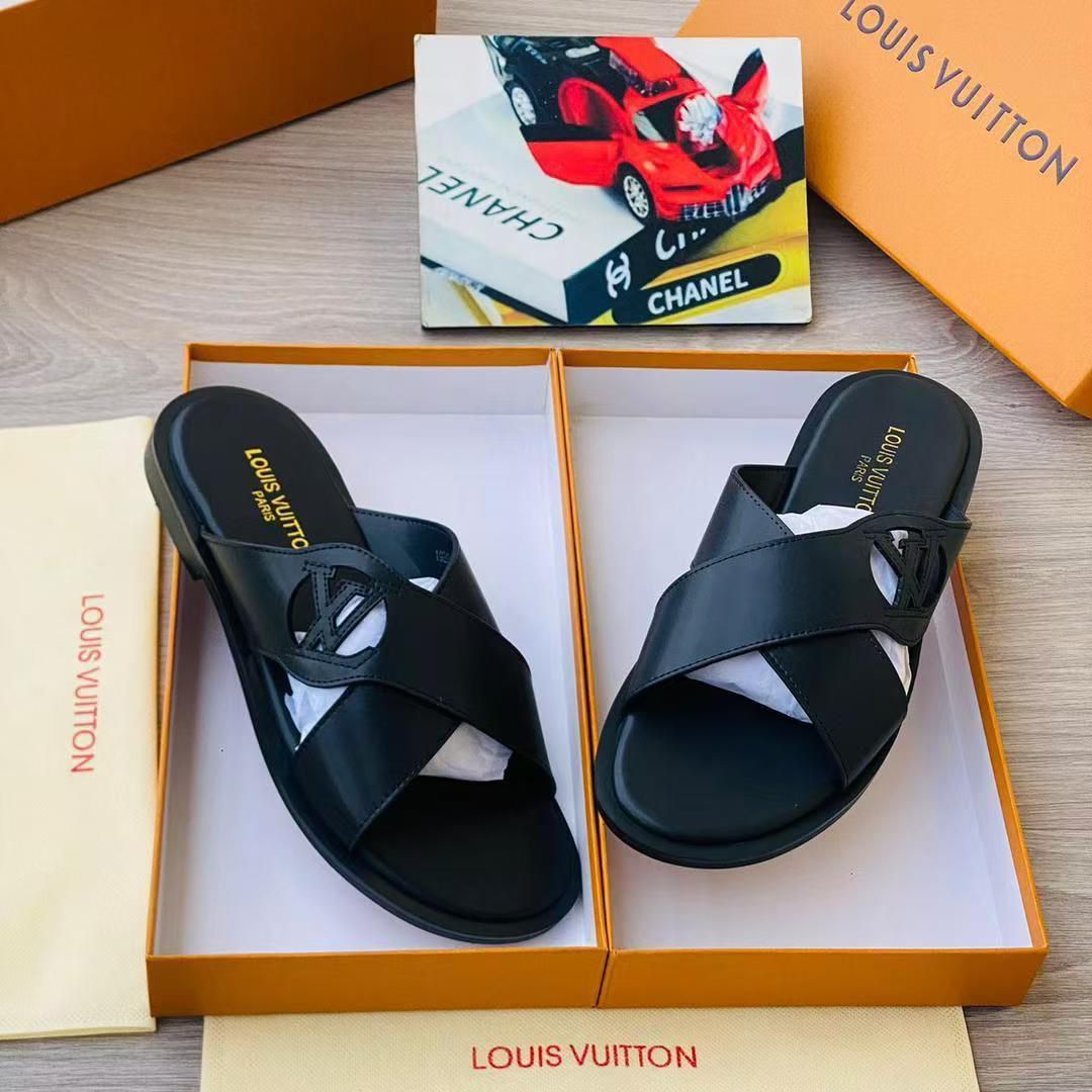 IMG-20260425-WA0042 A pair of black leather Louis Vuitton slide sandals with gold-toned logo, presented in an open orange box with white interior and accompanied by a dust bag.