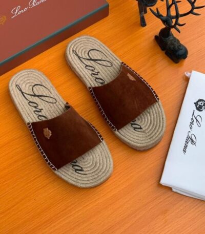 A pair of luxurious brown leather slide sandals with jute soles and Loro Piana branding on a wooden table with packaging and accessories.