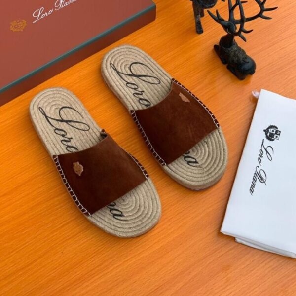 A pair of luxurious brown leather slide sandals with jute soles and Loro Piana branding on a wooden table with packaging and accessories.