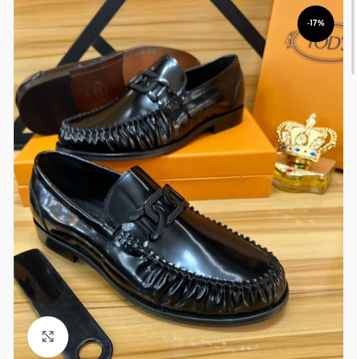 IMG-20260425-WA0051 A pair of black leather tassel loafers with fringed details, displayed on a wooden surface with a shoe box and accessories in the background.