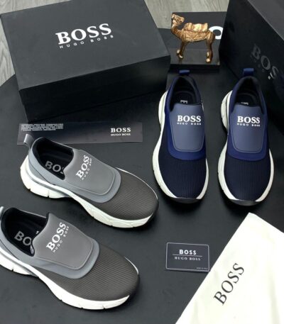 A display of Hugo Boss men's slip-on sneakers in navy blue and grey, accompanied by their original boxes and packaging.