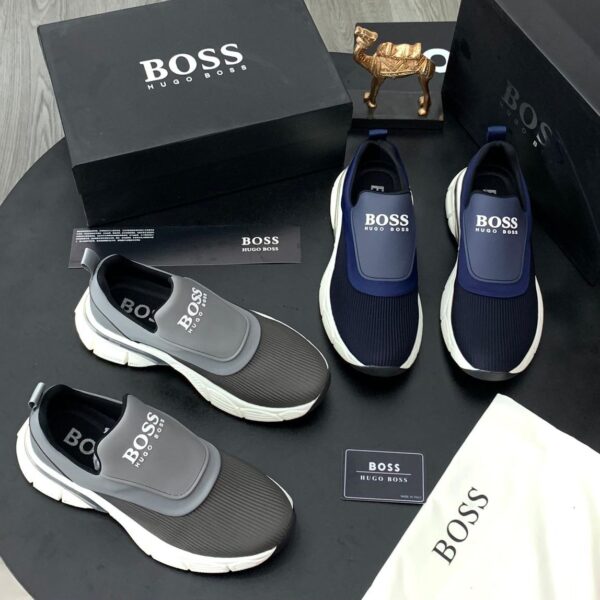A display of Hugo Boss men's slip-on sneakers in navy blue and grey, accompanied by their original boxes and packaging.