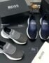 A display of Hugo Boss men's slip-on sneakers in navy blue and grey, accompanied by their original boxes and packaging.