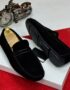 A pair of black suede loafers on a white box with a red carpet background, showcasing the shoes' sleek design and luxurious suede material.