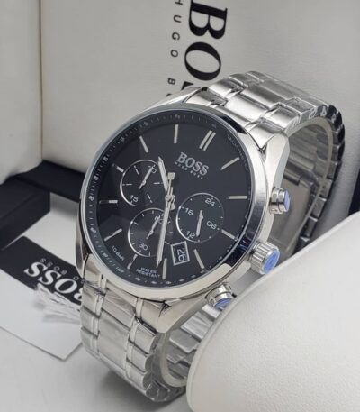 A close-up view of a Hugo Boss men's watch with a silver-toned stainless steel band and black dial, displayed on a white surface with the brand's packaging in the background.
