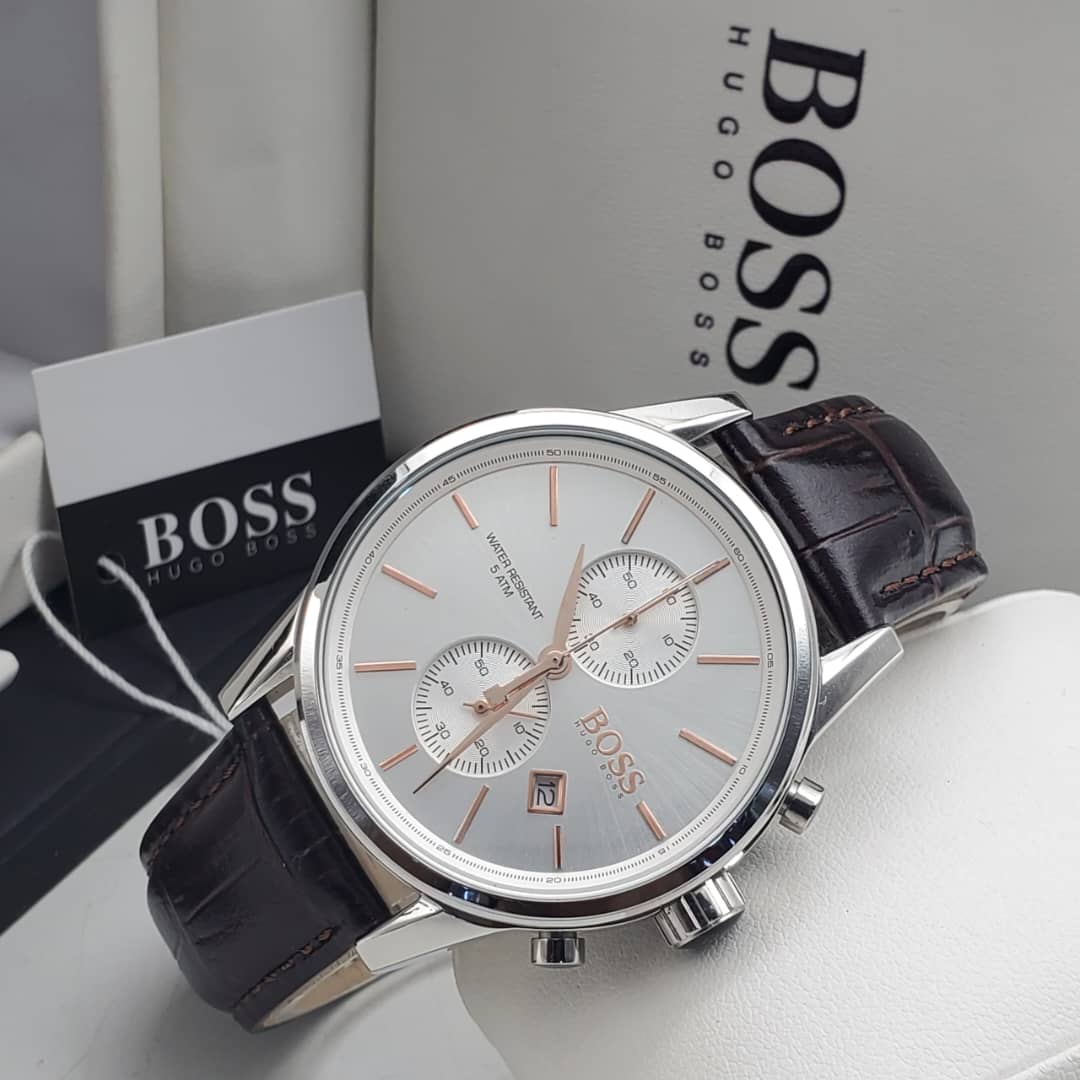 IMG-20260612-WA0008 A close-up of a Hugo Boss men's watch with a silver-toned case, white dial, and brown leather strap, displayed on a white surface with the brand's packaging in the background.