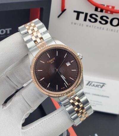 A close-up of a hand in a white glove holding a Tissot two-tone watch with a brown dial, showcasing its intricate details and luxurious design.