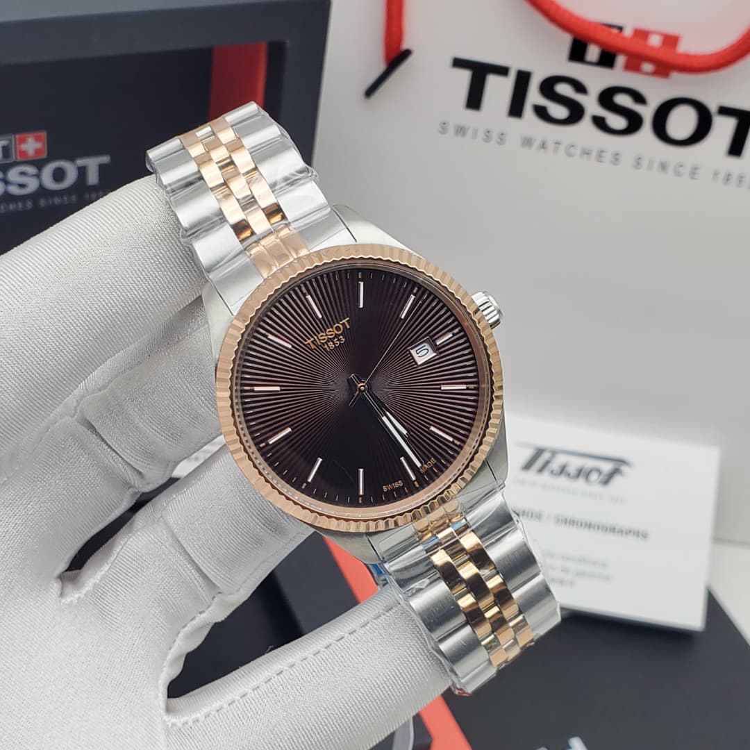 IMG-20260612-WA0010 A close-up of a hand in a white glove holding a Tissot two-tone watch with a brown dial, showcasing its intricate details and luxurious design.
