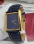 A luxurious Cartier Tank watch with a navy blue dial and gold accents, paired with a sleek leather strap, exuding high-end style and sophistication.