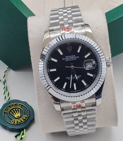 A luxurious Rolex Oyster Perpetual Datejust men's watch with a black dial and silver band, displayed on a white cushion with a green box and Rolex logo in the background.