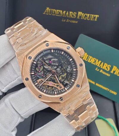 A close-up view of a rose gold Audemars Piguet Royal Oak Skeleton watch with an exposed movement, held by a gloved hand against a backdrop of the brand's packaging.