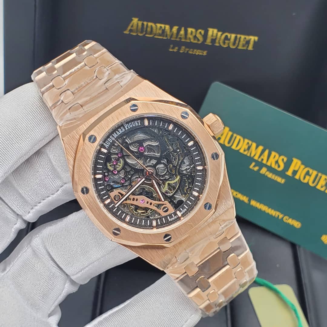 IMG-20260612-WA0027 A close-up view of a rose gold Audemars Piguet Royal Oak Skeleton watch with an exposed movement, held by a gloved hand against a backdrop of the brand's packaging.