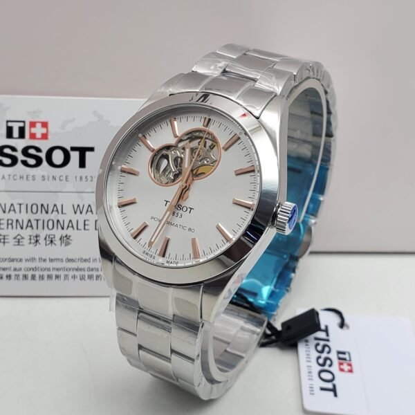 A sleek Tissot watch with a silver band and white face, featuring a visible mechanical movement, displayed on a white background with its box and tag.